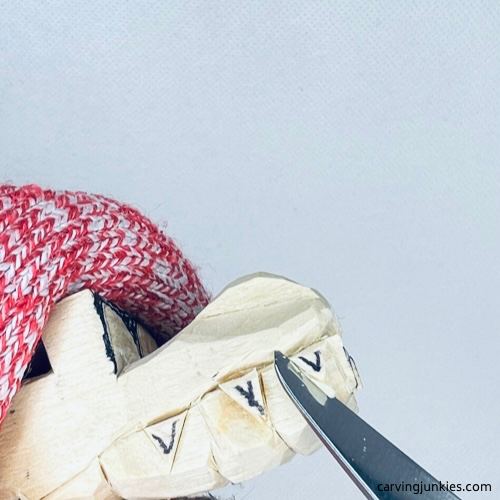 Carving teeth with a knife on wooden alligator