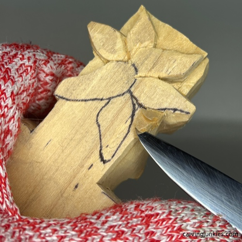 Shaping flower with a roughout knife on the back of a wooden cross wood carving