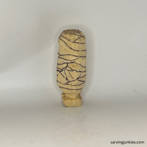 Bandages drawn on left side of wood carved mummy Details drawn on left side of wooden mummy carving